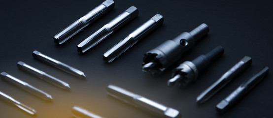Closeup straight flute tap tip and hole saw on dark background.  Industrial tapping tools. Carbide...