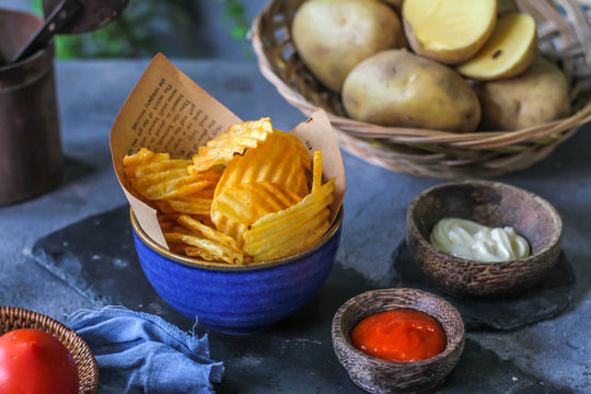 Photo of potato chips in a bowl with chili sauce on dark background. Chili ketchup. Ingredients. On a wooden table. Retro background. Front view. Studio photography. Image.