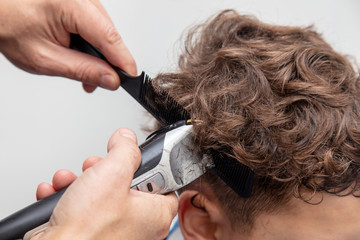 The hairdresser cuts the hair of a boy with a machine