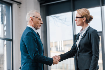 side view of businesswoman shaking hands with businessman in glasses