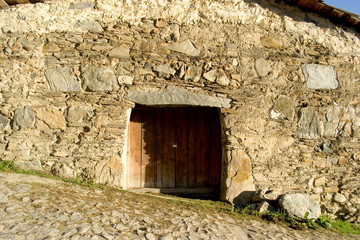 Fototapeta na wymiar Wooden doors to the ancient building in the georgian village Mestia. A wall of stones of various shapes, from small and flat, to huge rectangular stones. Beam from a single piece of rock.Street tilted