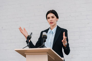 beautiful speaker gesturing and speaking near microphones