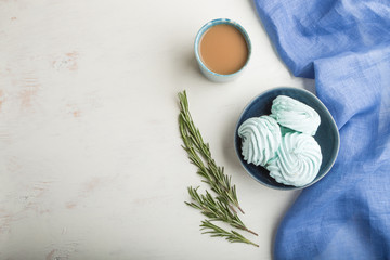 Blue colored homemade zephyr or marshmallow with cup of coffee on white wooden background. top view, copy space.