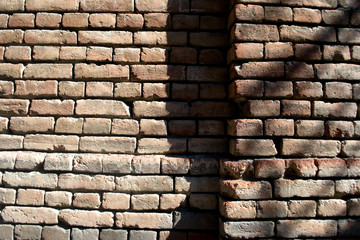 Part of the brick wall in the old town with a slight drop. From the drop a small shadow is formed. Different bricks, whole and slightly broken