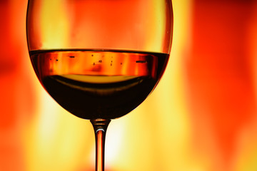 A glass of wine against the background of a burning fire. The atmosphere of rest and relaxation.