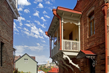 Unusual beauty of the balcony hanging over the old street. Balcony with white carved platbands, railings and columns. Beautiful red brick buildings and a clear blue sunny sky. Tbilisi, Georgia