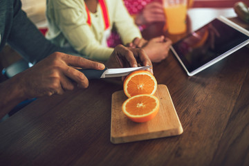 Hand slicing orange on wooden board.