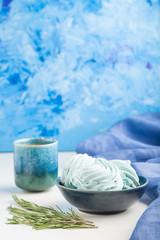 Blue colored homemade zephyr or marshmallow with cup of coffee on white wooden background. side view, selective focus, copy space.
