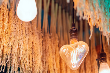 Antique heart shaped light bulbs hanging with green and gold color dried ear of rice to decorate in the coffee shop. Selective focus.
