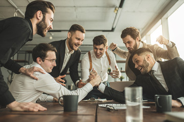 positive coworking business men in tuxedo, cheerfully playing arm wrestling after working day in office