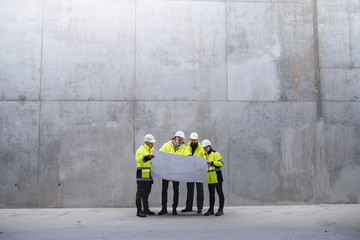 A group of engineers standing against concrete wall on construction site.