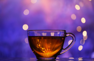 Transparent cup with black tea on a magical colorful background. The atmosphere of the holiday and winter travel.