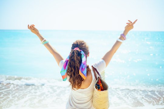 woman with beach straw bag with open arms rejoicing on seashore