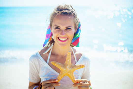 smiling young woman on ocean coast showing starfish - Powered by Adobe