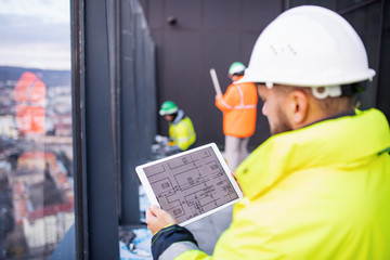 Man engineer standing on construction site, holding tablet.