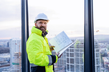 Man engineer standing on construction site, holding blueprints.