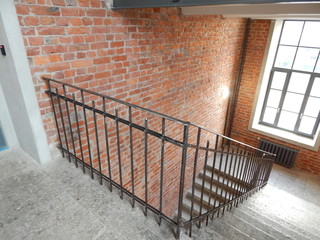 Old stone gray jagged staircase in the porch, red brick walls and cast-iron fencing