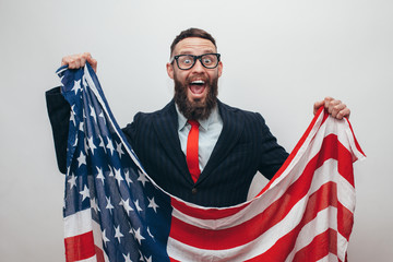 Handsome businessman with beard in trendy formal suit with American flag on gray background