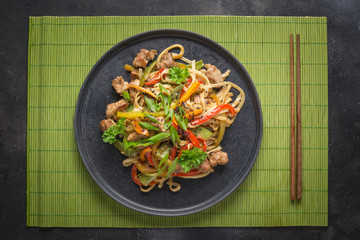 Udon stir-fry noodles with pork and chopsticks on black stone background. Asian cuisine.