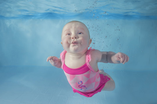 Little baby girl in pink swimsuit learns to swims underwater. Baby swimming underwater in the pool. Healthy family lifestyle and children water sports activity. Child development, disease prevention