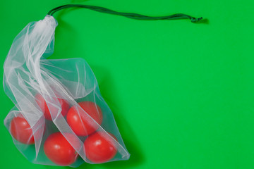 The reusable organza net bag for shopping with tomatoes is on the green background. Concept of no plastic, zero waste, reusable life. Flat lay. Copy space.