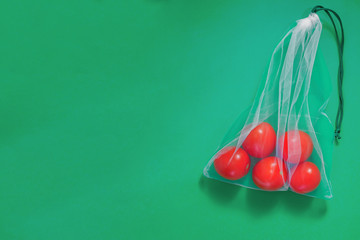 The reusable organza net bag for shopping with tomatoes is on the green background. Concept of no plastic, zero waste, reusable life. Flat lay. Copy space.