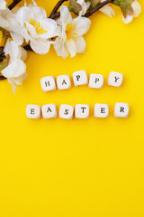 Happy Easter. Cubes with text on yellow background. Spring brunches with white flowers. Minimalistic flat lay.