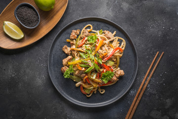 Udon stir-fry noodles with vegetables and pork on black stone background. Asian cuisine.