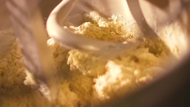 Close up for raw dough in a industrial bakery dough mixer, food concept. Stock footage. Top view of large stand machine used in commercial bakery to mix bread dough.