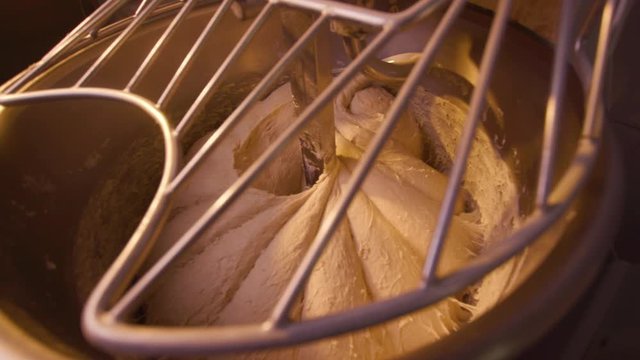 Close up for raw dough in a industrial bakery dough mixer, food concept. Stock footage. Top view of large stand machine used in commercial bakery to mix bread dough.