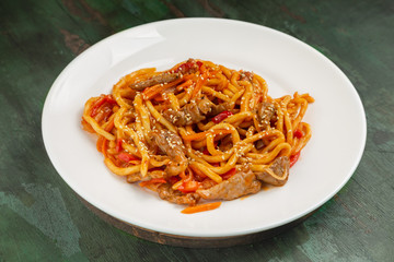 Wok noodles with meat and vegetables in a white plate on a wooden background