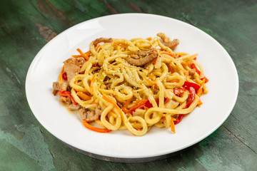 Wok noodles with meat and vegetables in a white plate on a wooden background