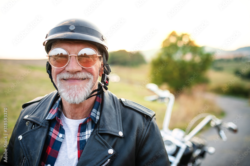 Wall mural a cheerful senior man traveller with motorbike in countryside, headshot.