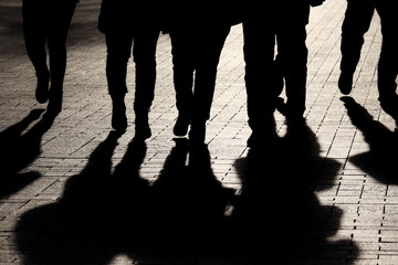 Silhouettes and shadows of people on the street. Crowd walking down on sidewalk, concept of...