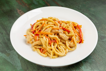 Wok noodles with meat and vegetables in a white plate on a wooden background