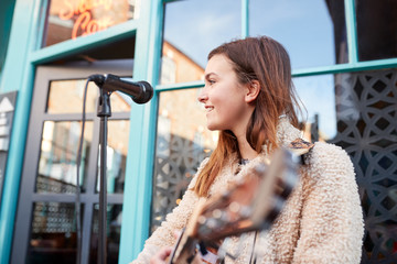 Female Musician Busking Playing Acoustic Guitar And Singing Outdoors In Street