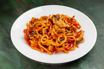 Wok noodles with meat and vegetables in a white plate on a wooden background