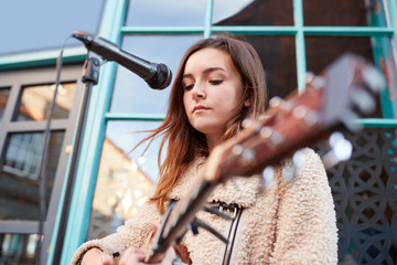 Female Musician Busking Playing Acoustic Guitar And Singing Outdoors In Street