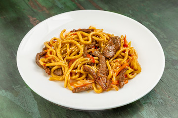 Wok noodles with meat and vegetables in a white plate on a wooden background
