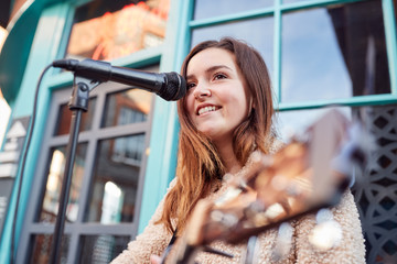 Female Musician Busking Playing Acoustic Guitar And Singing Outdoors In Street