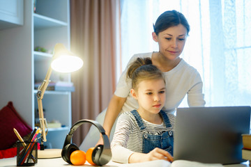 mother helping teen daughter studying computer while doing homework for school