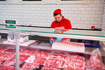 Butcher cutting raw lamb ribs behind the refrigerated display in a butcher shop