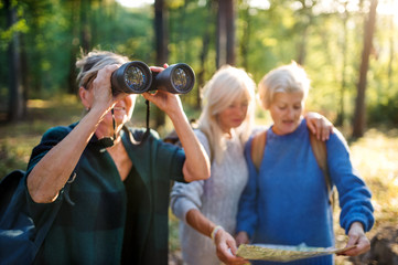 Senior women friends outdoors in forest, using map and binoculars.