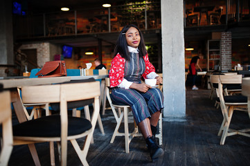 Fototapeta premium Сonfident young african american woman in smart casual wear at cafe with cup of hot drink in hand.