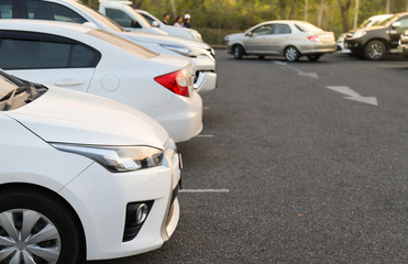 Fototapeta na wymiar Closeup of front side of white car and other cars parking in outdoor parking lot in the evening. 