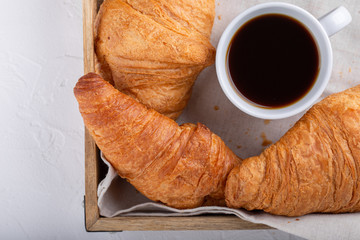 Cup of coffee and two croissants on wooden tray. Festive breakfast on white table. Top view, close-up.