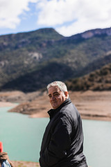 Fototapeta na wymiar Old man with gray hair with on a lake and mountains in the background