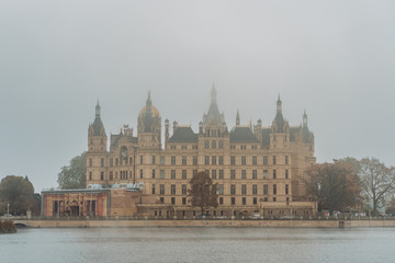 Fototapeta na wymiar Lake view of Side facade of Schwerin Castle Palace with heavy fog and haze in the morning