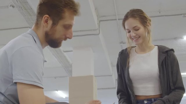 Male professional rollerblader helping young Caucasian woman putting protection on knees before training