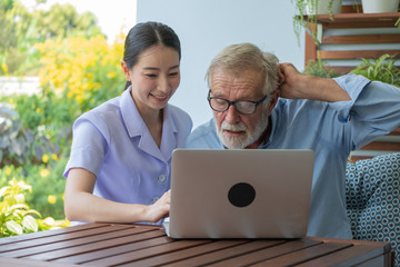 Obraz premium Young nurse take care senior man at home, Senior man with nurse are checking health results online by laptop, Health care concept